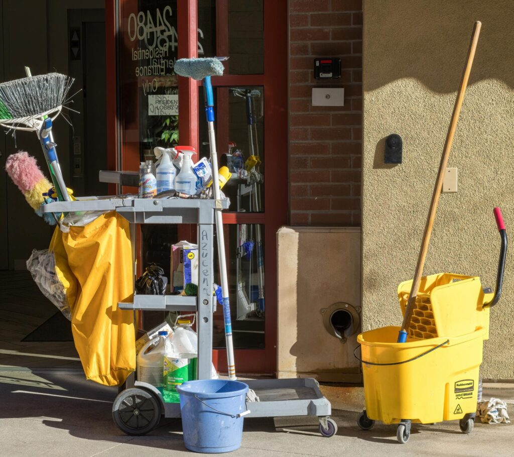pexels photo 17651101 17651101 Cleaning supplies and tools outside a building entrance bathed in sunlight.